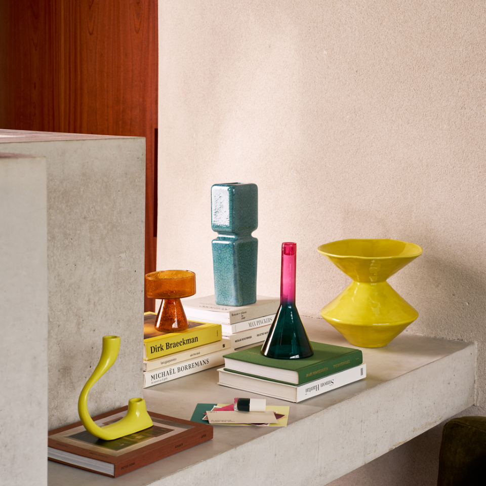 Colorful vases and books on a shelf against a neutral wall.
