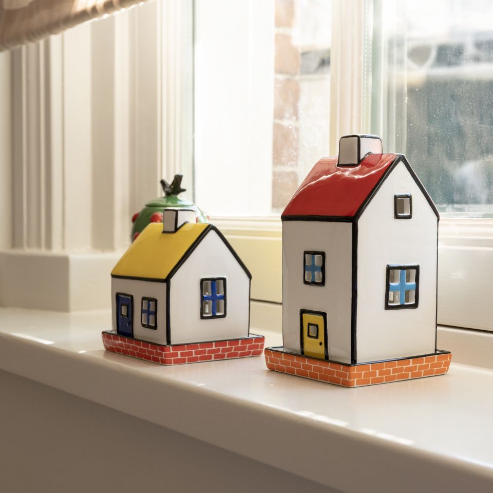 Two small house-shaped candle holders on a windowsill with a blurred background