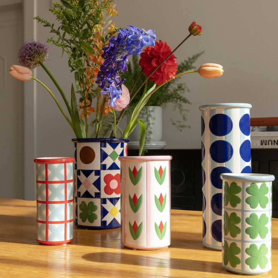 Set of colorful patterned vases with a vase containing flowers on a wooden surface.