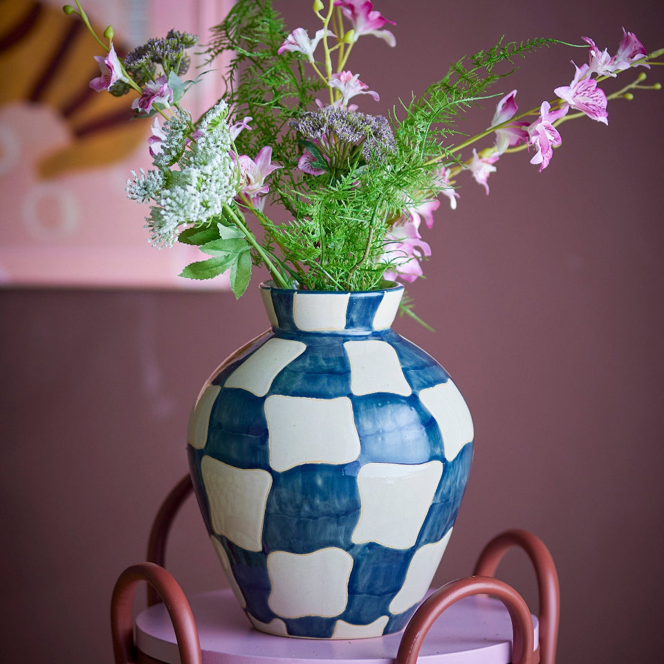 Navy and white checkered vase with flowers on a small round table against a pink wall.