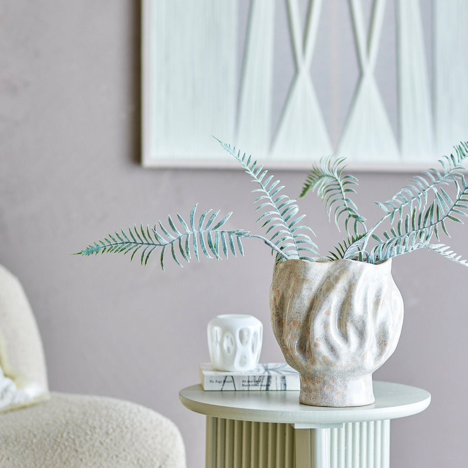 Decorative vase with greenery on a small round table against a gray wall.