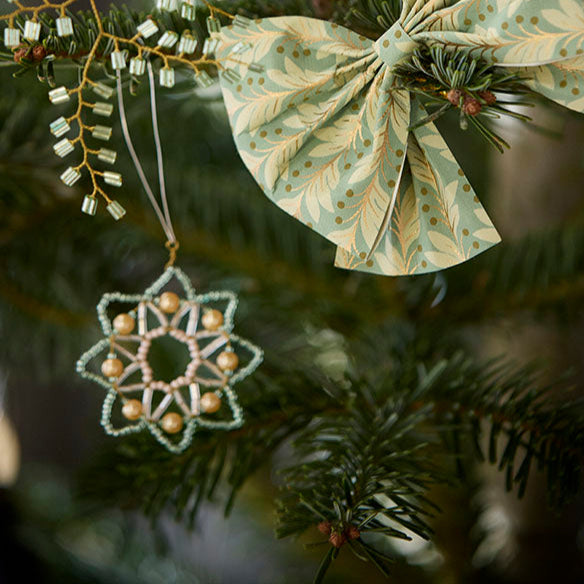 Decorative green bow and snowflake ornament on a Christmas tree.