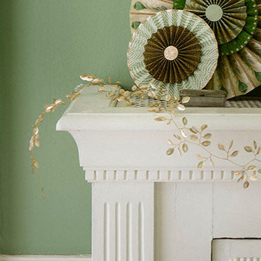 Decorative mantel with floral wreath, and decorations against a green wall.