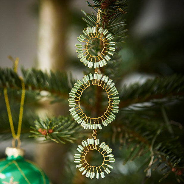 Decorative green ornament with gold  design hanging on a Christmas tree.