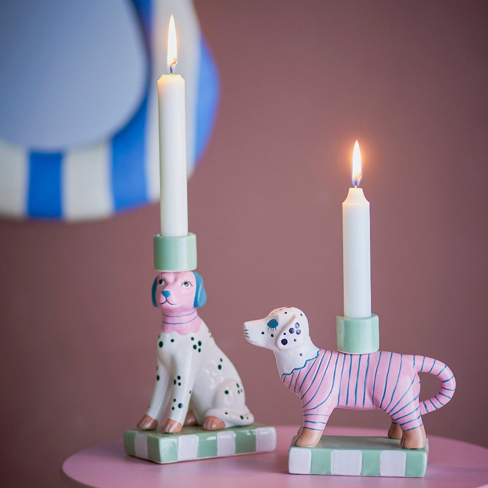 Two dog-shaped candle holders with lit candles on a pink surface.