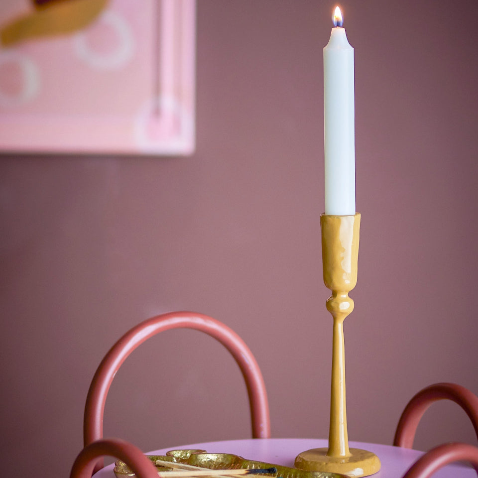 yellow candlestick with a lit white candle on a pink surface against a pink wall.