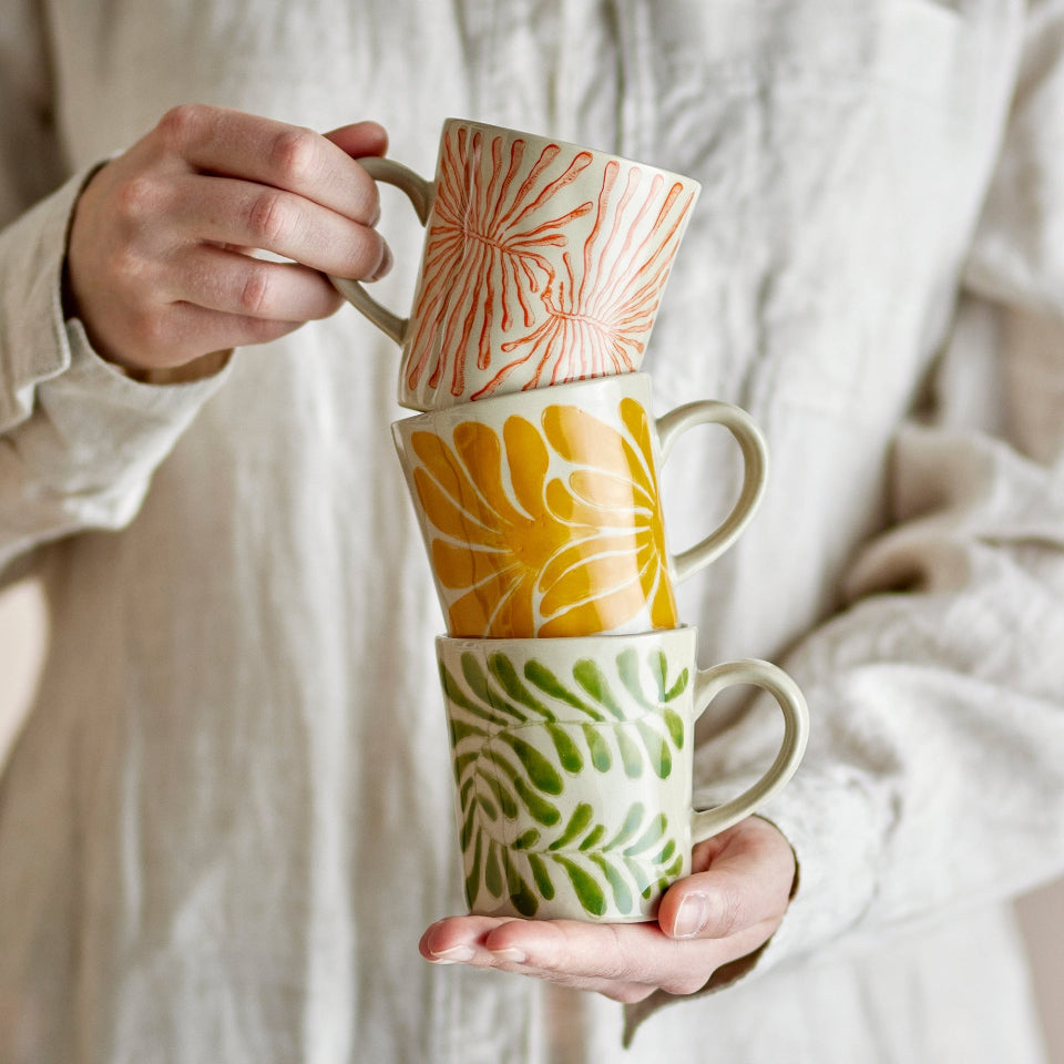 Stack of three ceramic mugs with floral patterns held by a person against a neutral background