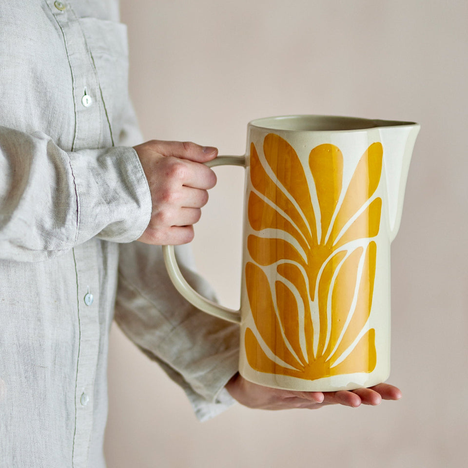 Person holding a ceramic pitcher with yellow leaf pattern on a beige background