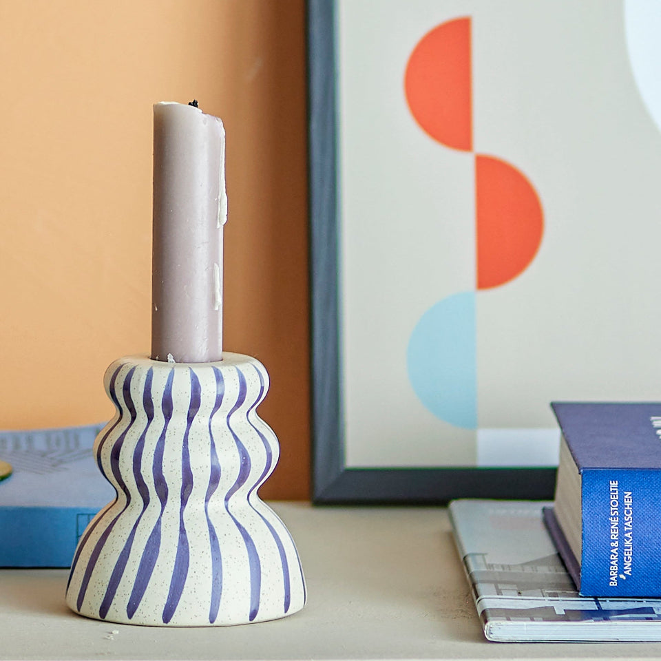 Decorative candle holder with wavy pattern on a surface with a colorful abstract painting in the background.