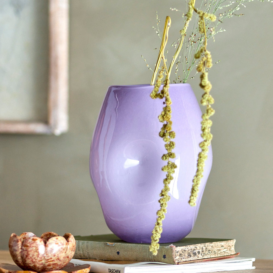 Purple vase with dried plants on a wooden surface against a neutral wall