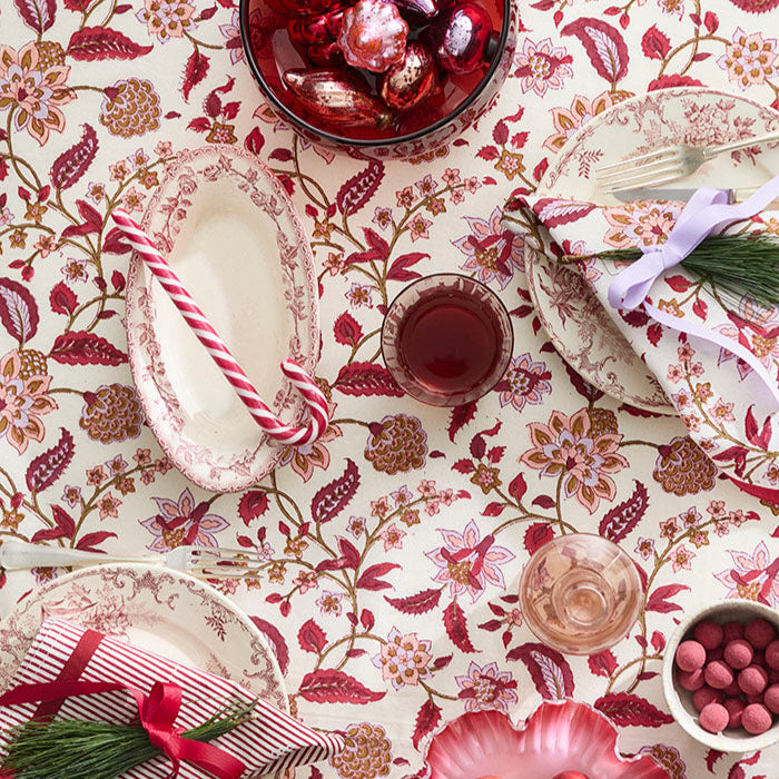 Decorative table setting with floral tablecloth, apples, and glasses on a patterned surface.