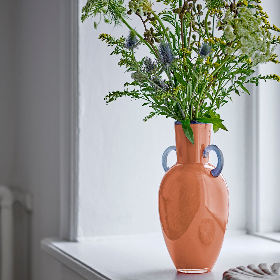 Orange Glass vase with floral arrangement on a windowsill