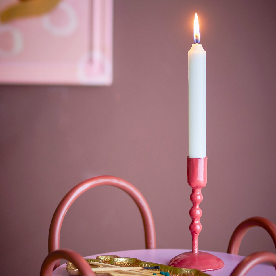 Red candle holder with a lit candle on a pink table against a pink wall.