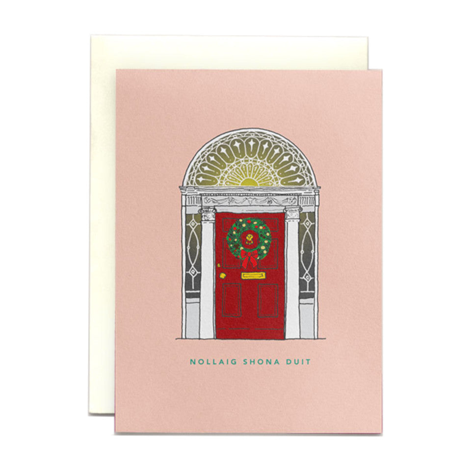 Red Dublin Georgian door and fanlight on a pink background Christmas card with 'Nollaig shona duit' (Happy Christmas to you) and a Christmas wreath hanging on the door.