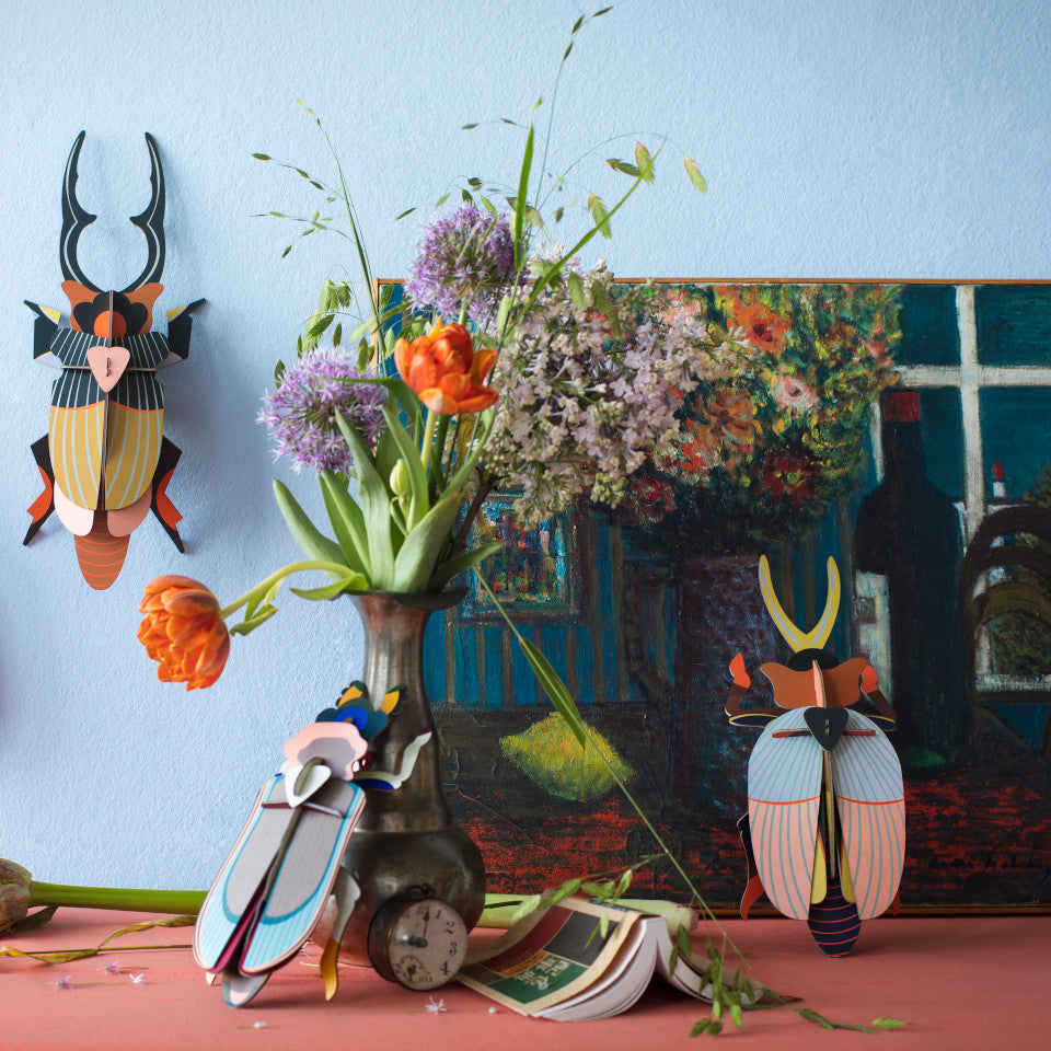 Giant Stag, Rhinoceros and Tiger beetle cardboard wall decorations, styled with a vase of flowers and a painting.