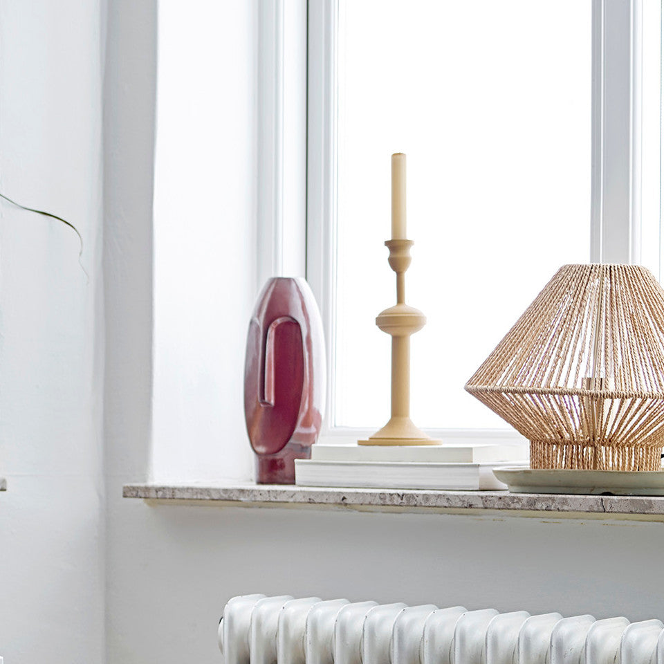 Idica candlestick, yellow metal in a 'turned wood' style, styled on a windowsill with other decorative items and books.