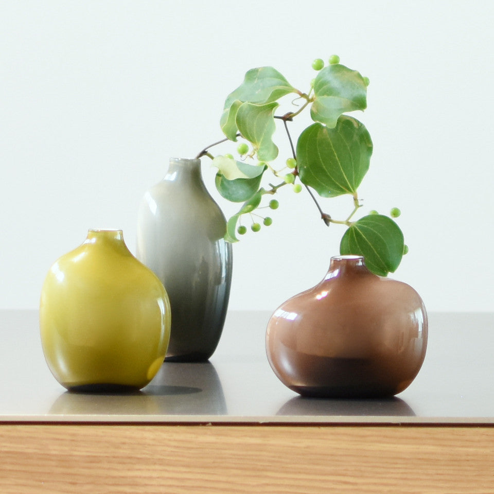 Sacco r-l, brown glass small vase, large grey glass and medium green glass vases, styled with foliage.