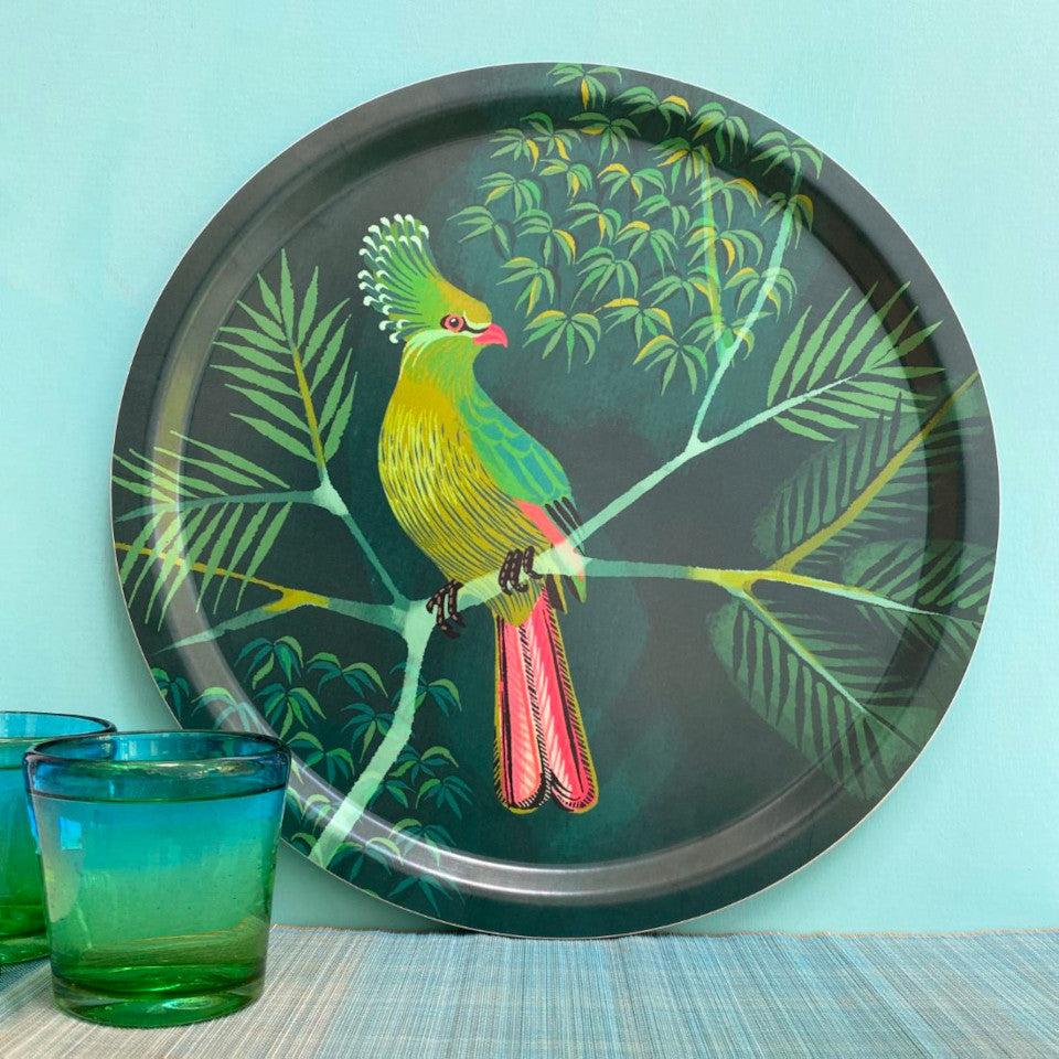 Turaco by Asta Barrington, turaco on tropical tree branch on green background, 39cm round tray, styled leaning against a mint green painted wall, with two green-blue drinking glasses.